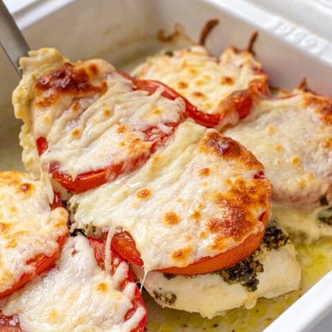 Spatula lifting a baked pesto chicken cutlet out of a dish, covered in melted mozzarella cheese.