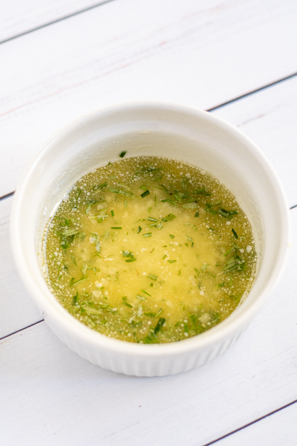 a small white bowl holding the melted butter mixture with garlic and chopped rosemary.
