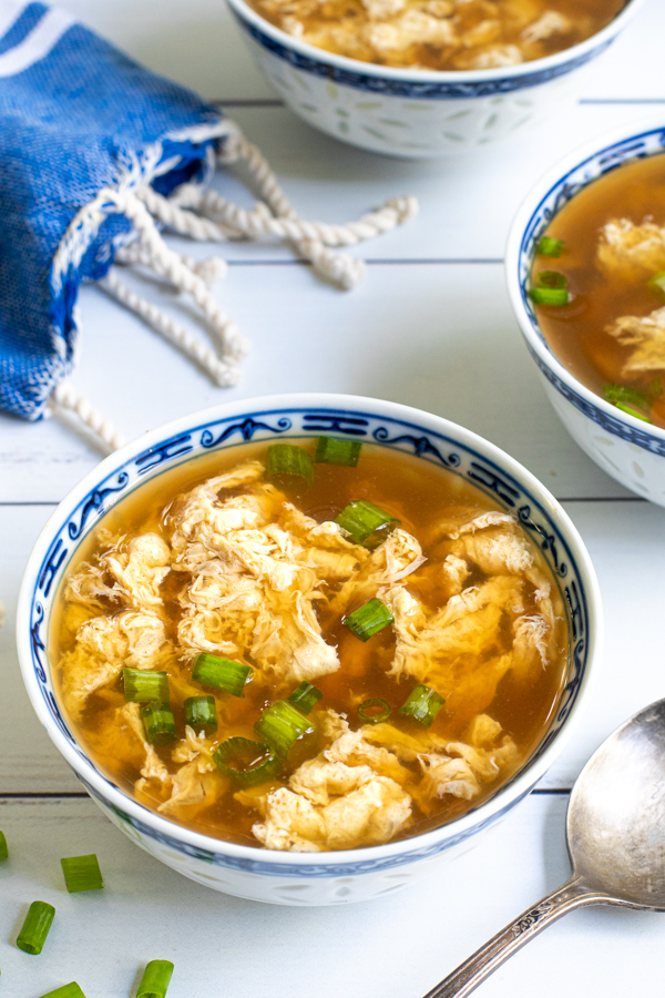 Close up of a bowl of egg drop soup showing silky egg ribbons in flavorful broth and garnished with green onions.