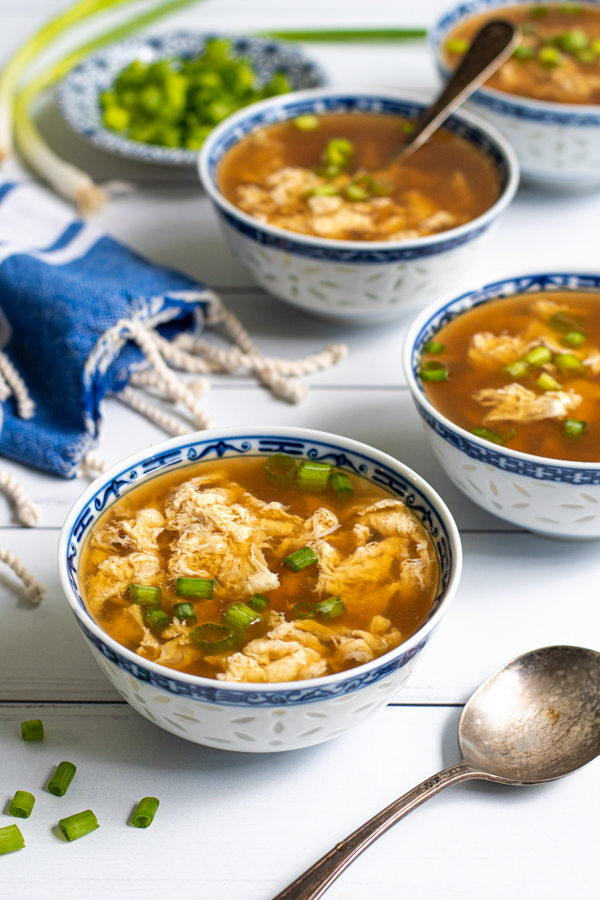 Four small Chinese blue and white bowls laid out on a table filled with egg drop soup and garnished with sliced green onions.