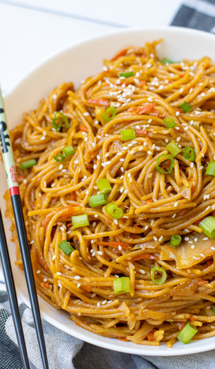 Freshly made Teriyaki Noodle Recipe in a large white bowl garnished with green onions and sitting next to a pair of chopsticks.