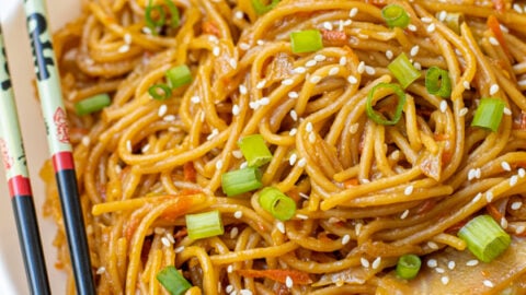 Freshly made Teriyaki Noodle Recipe in a large white bowl garnished with green onions and sitting next to a pair of chopsticks.