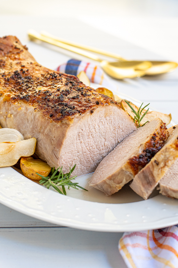 A sliced open pork loin on a serving platter with two sliced cut and showing of the center inside showing a slight pink center.