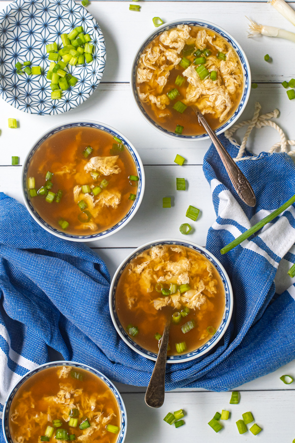 Overhead view of 4 blue and white Chinese bowls filled with egg drop soup and garnished with green onions.