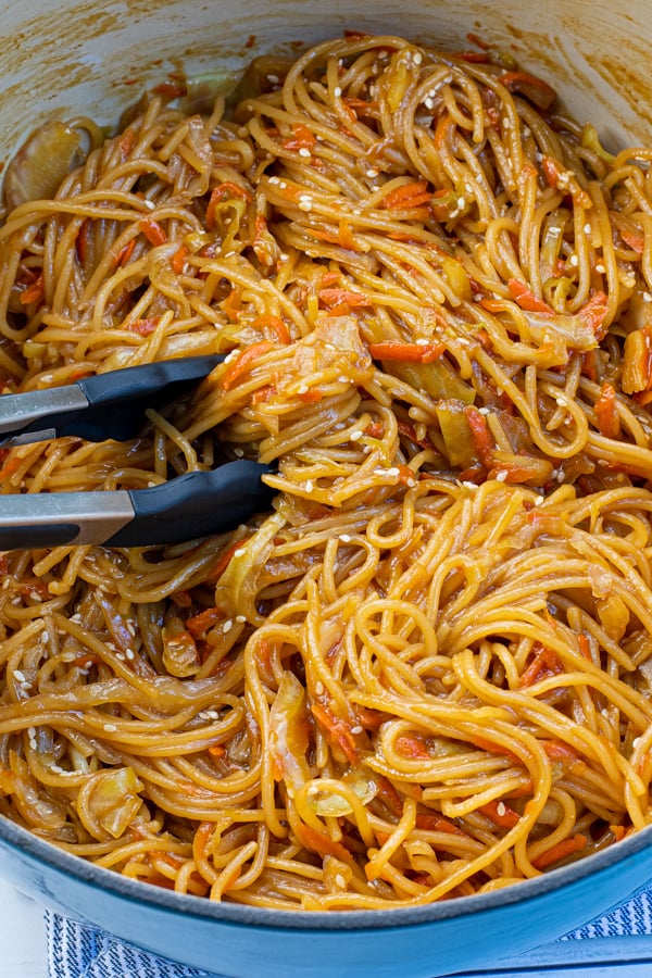 Close up of freshly cooked noodles in a large pot with a pair of tongs.