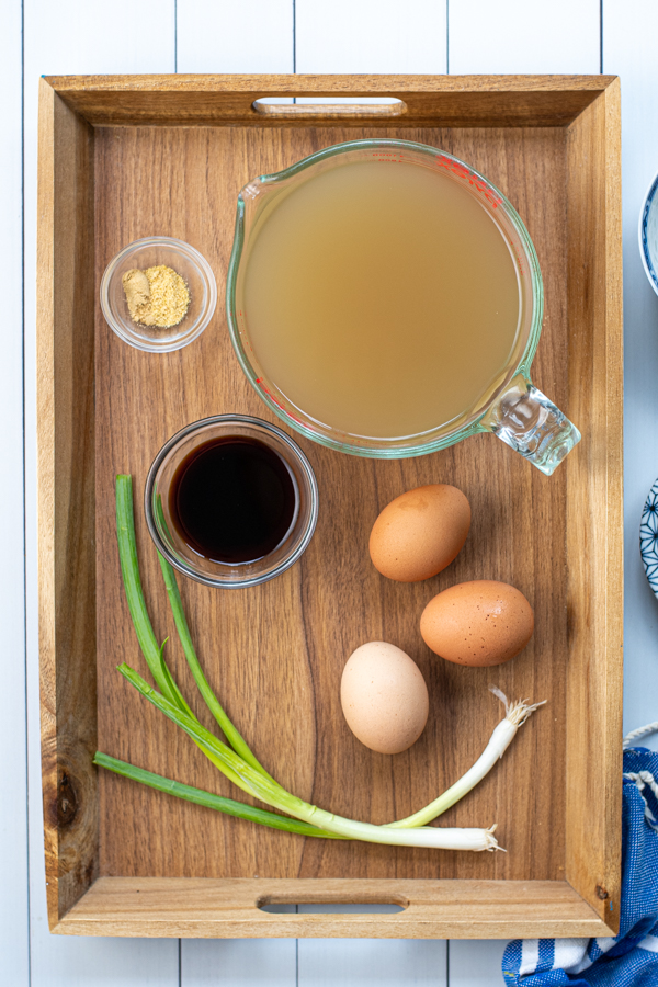 The simple ingredients needed to make egg drop soup sitting on a wooden tray.