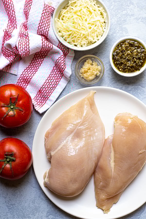Ingredients to make Pesto Chicken, chicken breasts, tomatoes, garlic, pesto, and mozzarella cheese.
