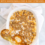 Pinterest Pin with Text: Sweet Potato Casserole with Marshmallow & Oat Streusel, showing a baking dish with sweet potato casserole with a gold serving spoon.