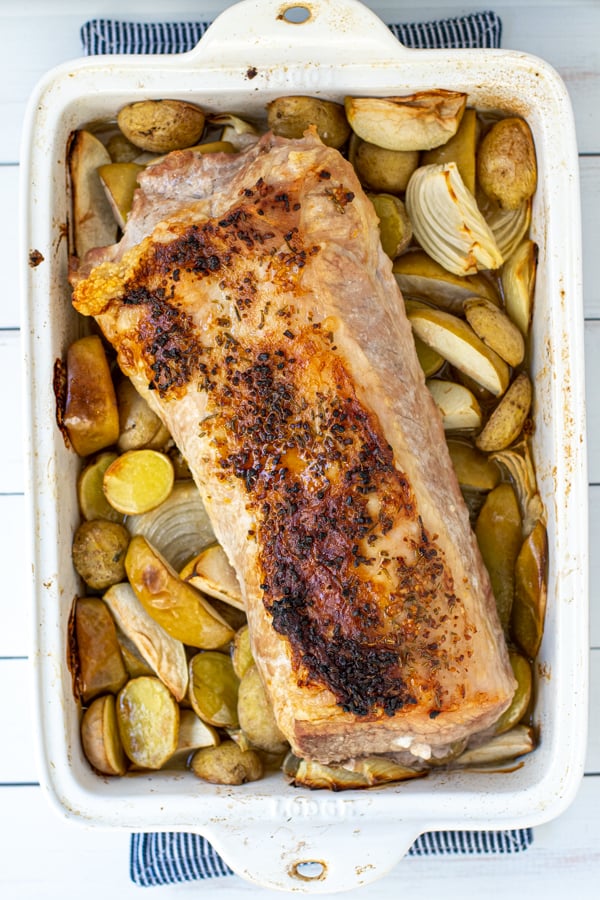 The pork roast freshly out of the oven, with a juicy brown crust next to browned potatoes and apples.