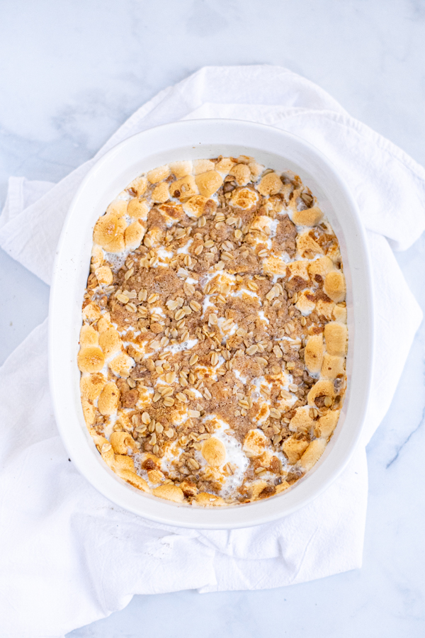 Overhead view of Sweet Potato Casserole with Marshmallows and Oat Streusel in a white baking dish on top of a white kitchen towel.