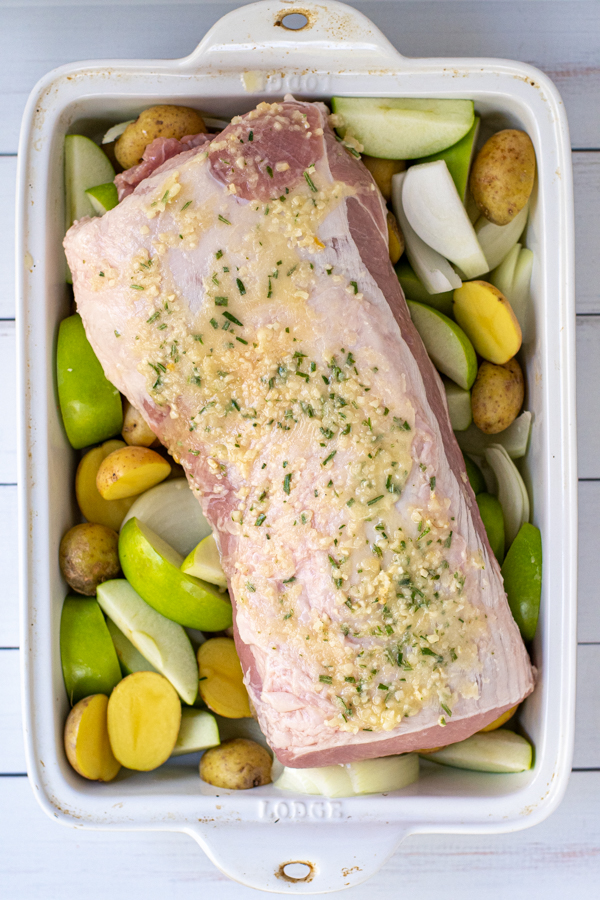 Overhead view of the pork loin ready to go in the oven with the apples and potatoes with the garlic butter mixture drizzled on top.