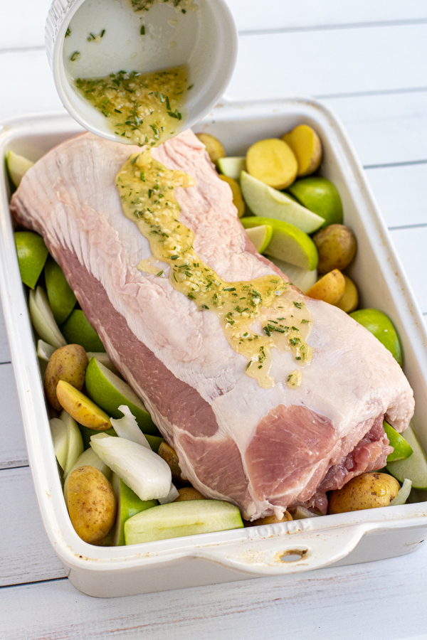 Butter mixture with fresh rosemary being poured over top of a pork loin in a baking dish.