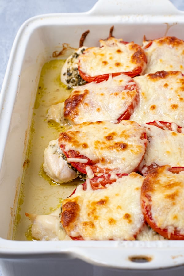 side view of a white baking dish with baked pesto chicken topped with mozzarella cheese.
