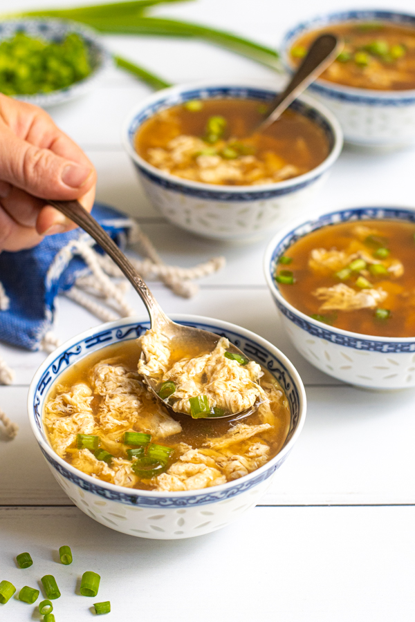 A spoon in a bowl of egg drop soup, garnished with green onions.