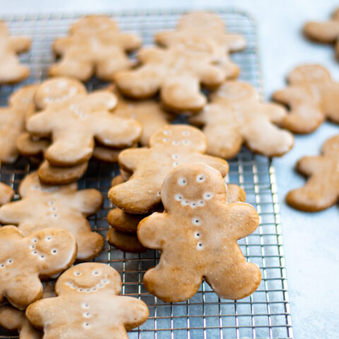 A bunch of gingerbread men on a wire cooling rack, one of the cookies is standing up showing off the glazed front.