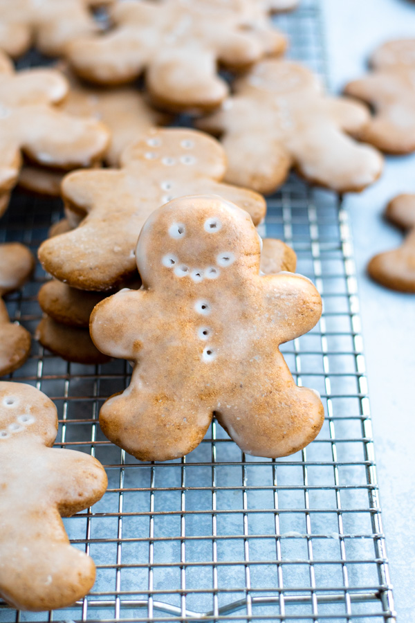 A glazed gingerbread cookie tilted up leaning against a stack of more cookies on a wire cooling rack.