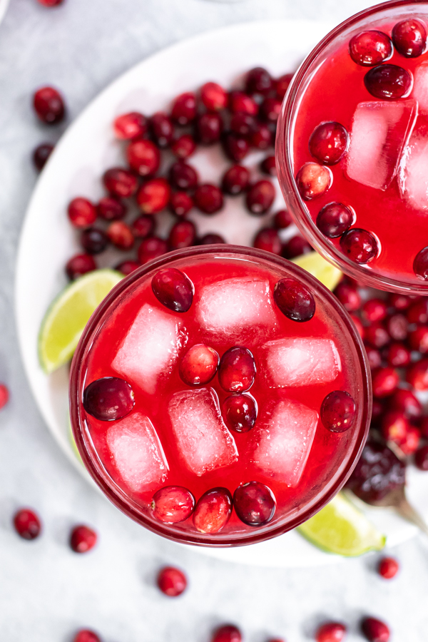 Close up of a glass filled with red cranberry sauce margarita, fresh cranberries, and ice.