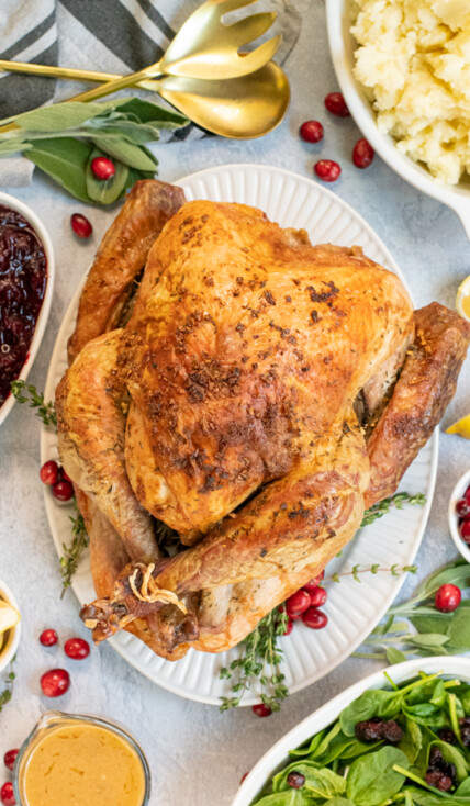 Overhead view of a full thanksgiving table with the roasted turkey in the center with crispy golden brown skin from dry brining on a large platter.