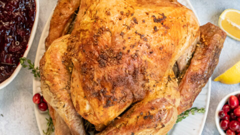 Overhead view of a full thanksgiving table with the roasted turkey in the center with crispy golden brown skin from dry brining on a large platter.