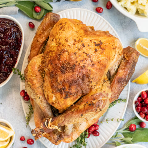 Overhead view of a full thanksgiving table with the roasted turkey in the center with crispy golden brown skin from dry brining on a large platter.