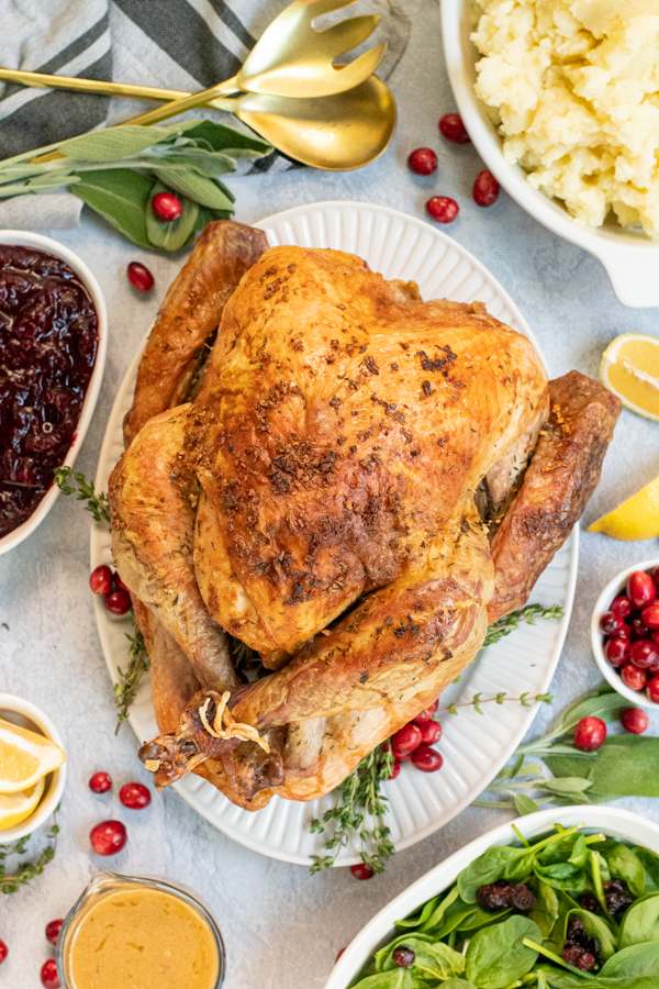 Overhead view of a full thanksgiving table with the roasted turkey in the center with crispy golden brown skin from dry brining on a large platter.