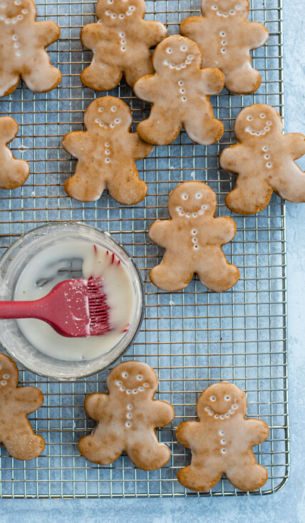 Soft Glazed Gingerbread Cookies arranged out on a wire cooling rack with a bowl and brush full of glaze.