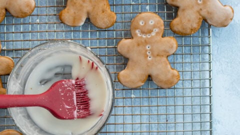 Soft Glazed Gingerbread Cookies arranged out on a wire cooling rack with a bowl and brush full of glaze.