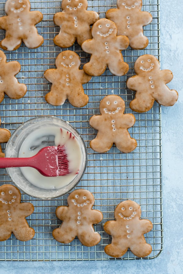 Soft Glazed Gingerbread Cookies arranged out on a wire cooling rack with a bowl and brush full of glaze.
