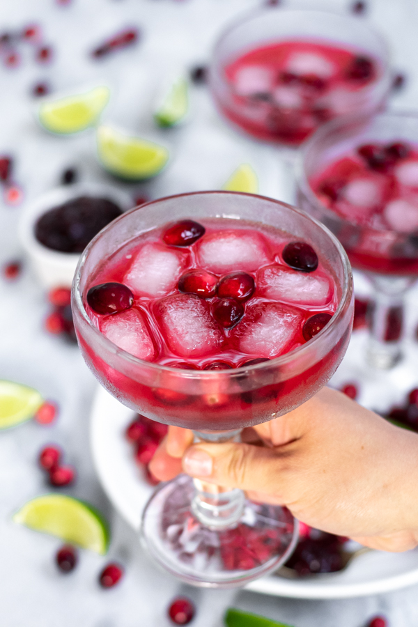 Hand holding a margarita glass filled with a bright red drink and garnished with fresh cranberries.