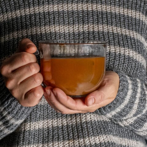 Hands holding a clear mug full of hot toddy with tea.