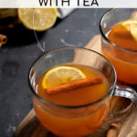 Pinterest Pin with text overlay 'How to make a Hot Toddy with Tea'. Image of a clear mug filled with hot toddy and garnished with a cinnamon stick and lemon slice.