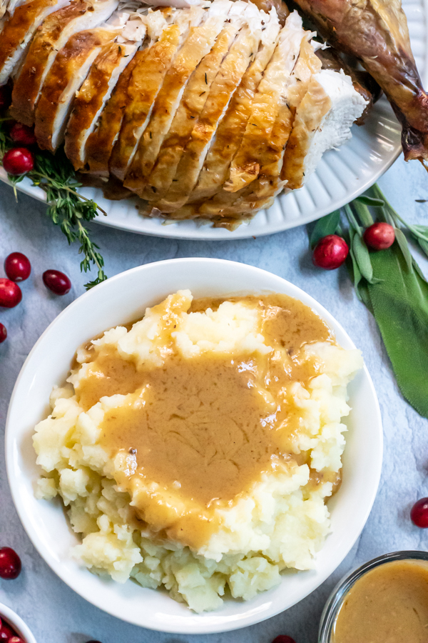 Flatlay of a huge bowl of mashed potatoes smothered in turkey gravy next to a platter of thanksgiving turkey.