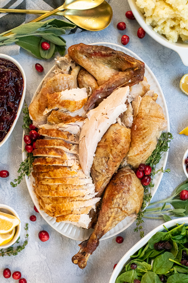 Overhead of a large white platter with fully carved dry brined turkey laid out.