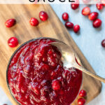 Pinterest Pin with text: How to make Homemade Cranberry Sauce. Image of bowl of cranberry sauce next to loose cranberries with a spoon.