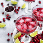 Pinterest Pin with text overlay, Cranberry Sauce Margaritas, image shows three glass filled with a bright red margarita and table filled with fresh cranberries.