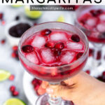 Pinterest Pin with text overlay, Cranberry Sauce Margaritas, image shows hand holding a red margarita garnished with fresh cranberries and ice.