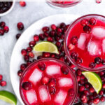 Pinterest Pin with text overlay, Cranberry Sauce Margaritas, image shows overhead view of bright red margaritas garnished with fresh cranberries and ice.