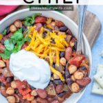 Pinterest Pin with text overlay, Three Bean Chili. Image of a white bowl of chili with a spoon full of chili roasting on the side showing off the three different kinds of beans used.