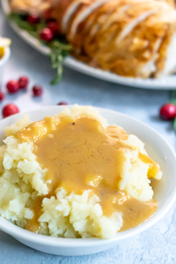 A large pool of turkey gravy made from drippings in a large bowl of mashed potatoes sitting on a thanksgiving table.