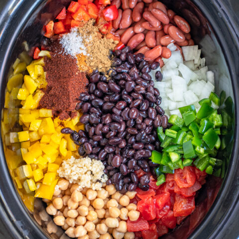 All of the ingredients for easy vegetarian chili laid out nicely in the black crock of a slow cooker.
