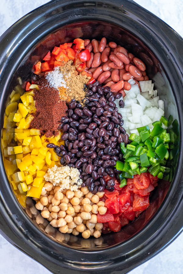 All of the ingredients for easy vegetarian chili laid out nicely in the black crock of a slow cooker.