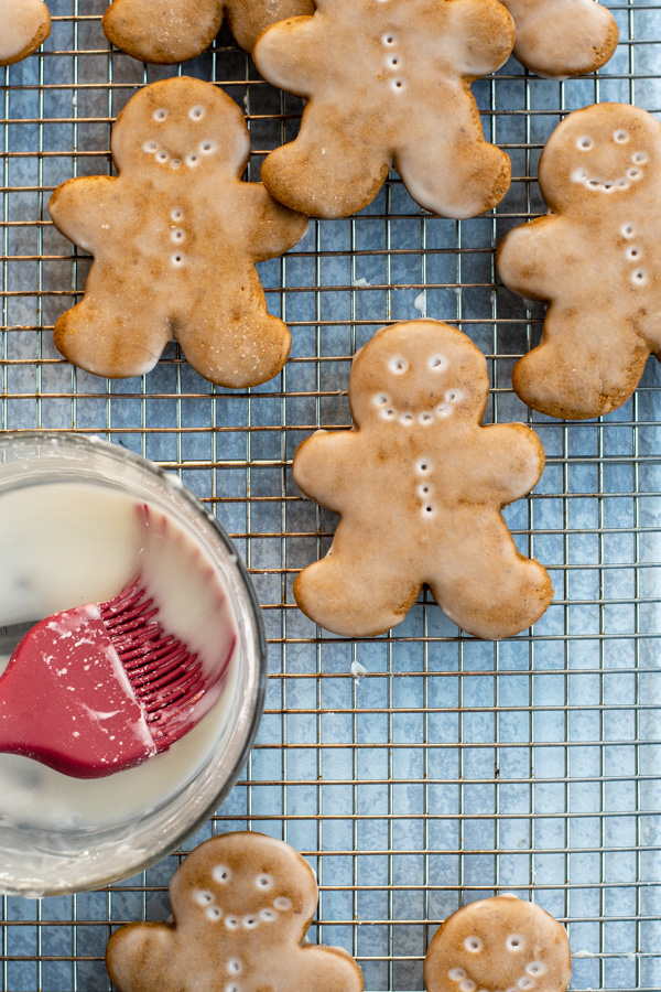 Glazed Gingerbread Cookies arranged on a wire cooling rack with a bowl full of glaze.