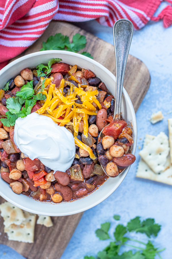 A spoon full of three bean chili roasting on the side of a white bowl full of chili.