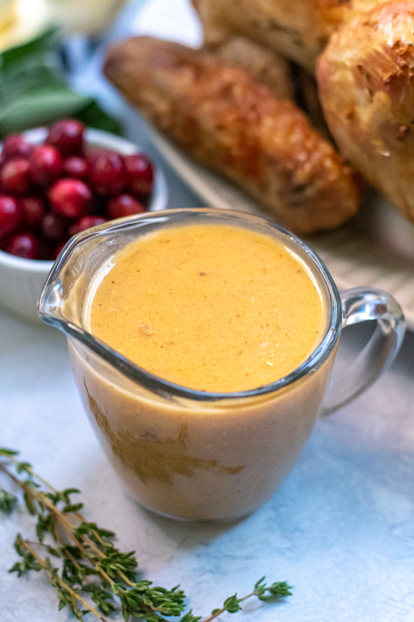 Turkey gravy from drippings in a glass creamer on a thanksgiving table next to a roast turkey and cranberries.