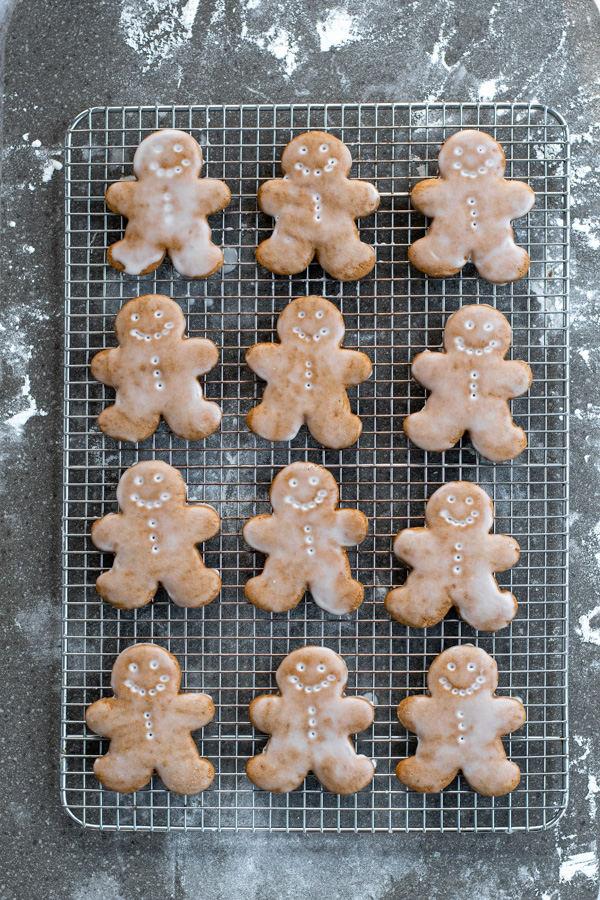 A wire cooling rack full of freshly glazed gingerbread cookies showing off the face and button designs.