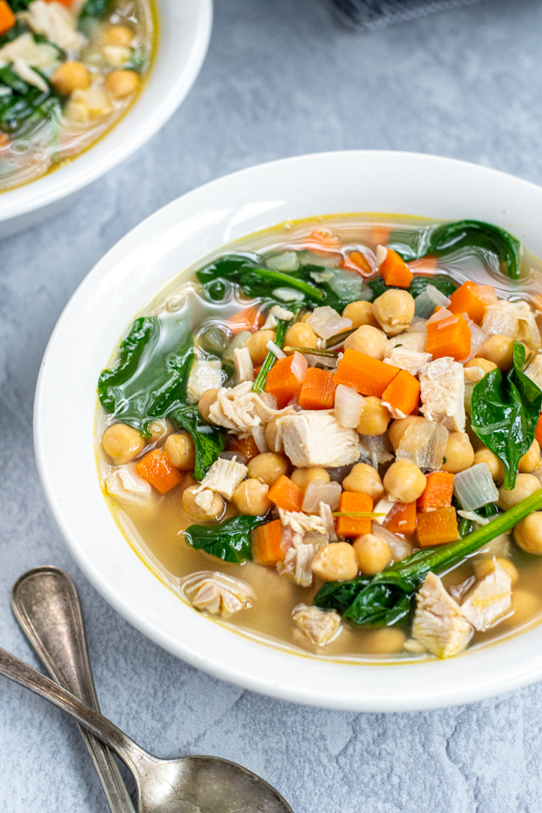 Close up on a white bowl filled with turkey soup with carrots, beans, and healthy spinach.