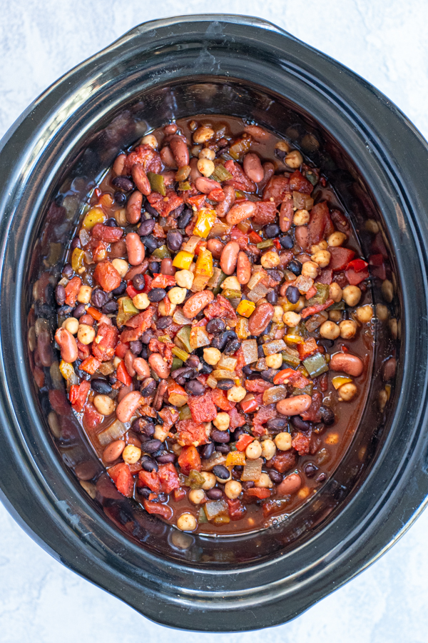 An overhead view of a crockpot filled with freshly cooked vegetarian chili showing off bright peppers and lots of beans.