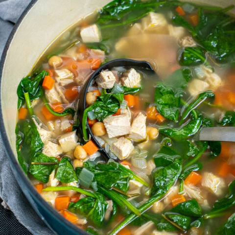 Ladle in a pot of healthy leftover turkey soup filled with chunks of turkey, spinach, chickpeas, and carrots.