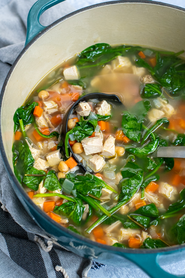 Ladle in a pot of healthy leftover turkey soup filled with chunks of turkey, spinach, chickpeas, and carrots.