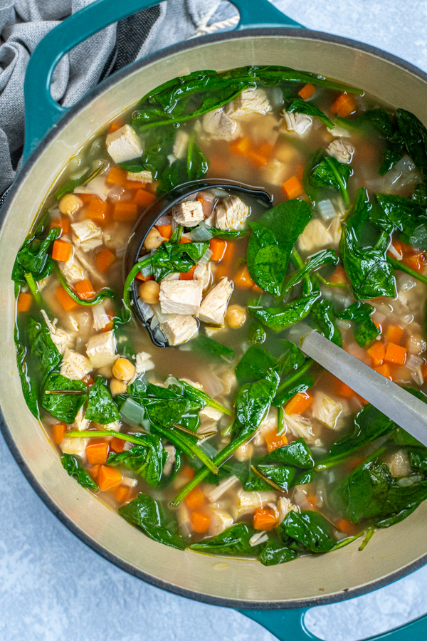 Large dutch oven filled with a colorful turkey soup including turkey chuck, bright spinach, and diced carrots.